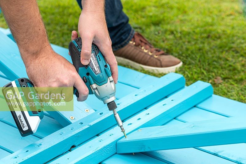 Man assembling a picnic bench - fixing cross bar diagonally to stabilise the structure