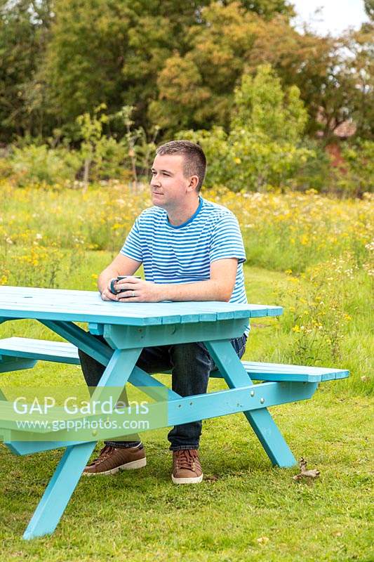 Man sitting at newly assembled picnic bench in meadow