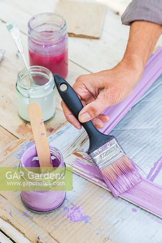 Woman painting a frame in a light shade of purple using a paint brush