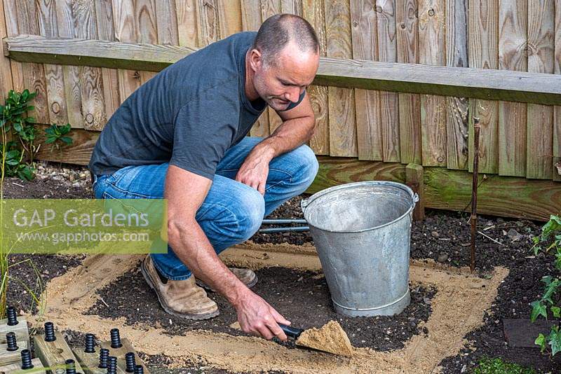 Having levelled the ground, man sprinkles soft builder's sand ready to receive the bottom layer of timber for raised bed.