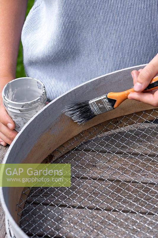 Woman painting wooden sieve with outdoor paint.  Planting Succulent Sieve.  Step 1.