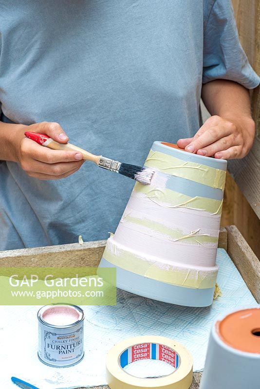 Using masking tape to cover create stripes, painting the remainder of the pot with a second, contrasting colour.
