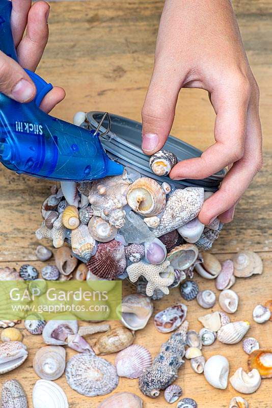 Building up a coat of shells, using a hot glue gun to secure each in place on a plastic plant pot