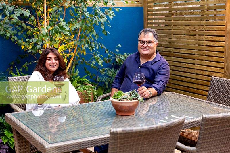 Small garden in West London with owners Noreen and Fawad Ahmad sitting at a table in the patio area. 