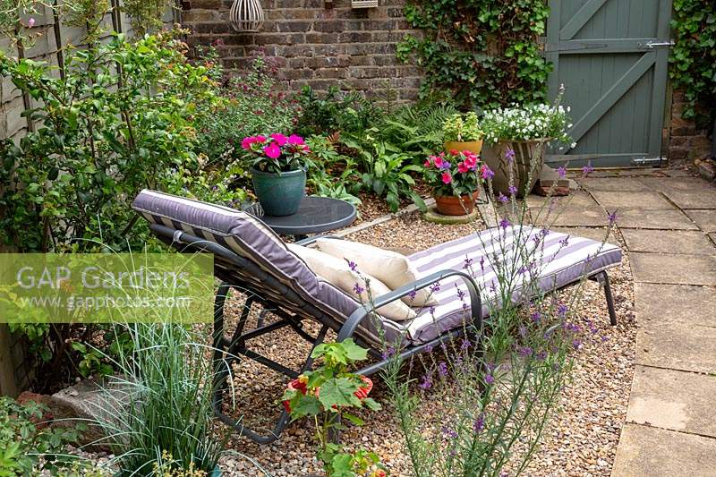 Gravel patio with sun lounger with summer bedding in containers