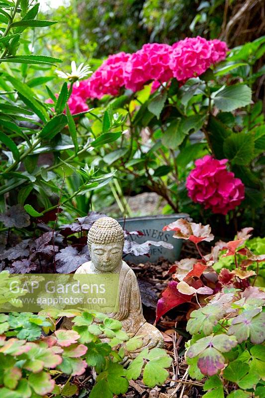 Herbaceous border with small Buddha statue