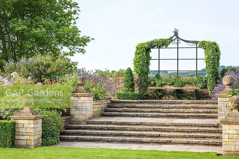 Steps leading up from the lawn to a raised walk with ivy covered arbours at Bourton House