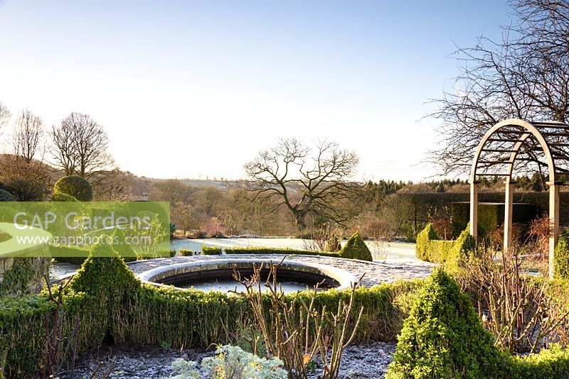 A circular pond set into a formal terrace is surrounded by low Buxus - Box -hedging and planting in a country garden 