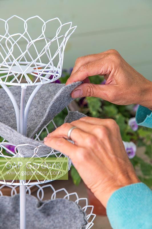 Woman adding the grey felt lining to the tiered metal planter. 