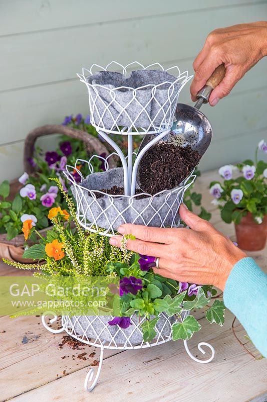 Woman adding compost to tiered metal planter. 