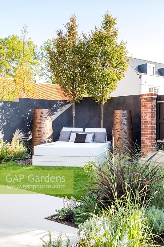 Modern white outdoor double daybed with large Torc pots and backed by dark fencing. 