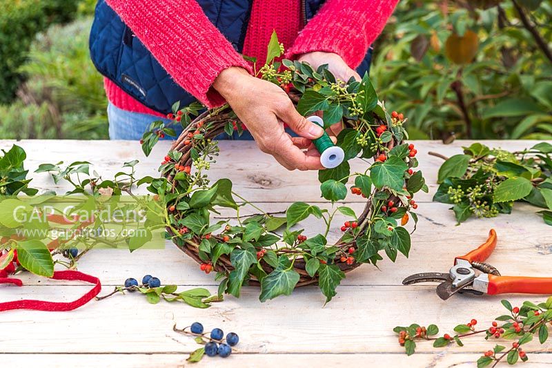 Woman using floristry wire to fasten Ivy - Hedera to wreath