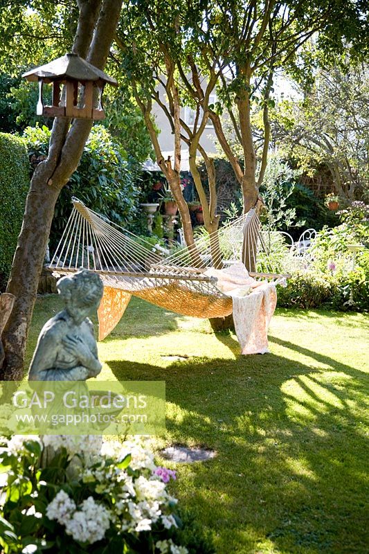 Large hammock with blankets hanging between trees in garden, sculpture in foreground 
