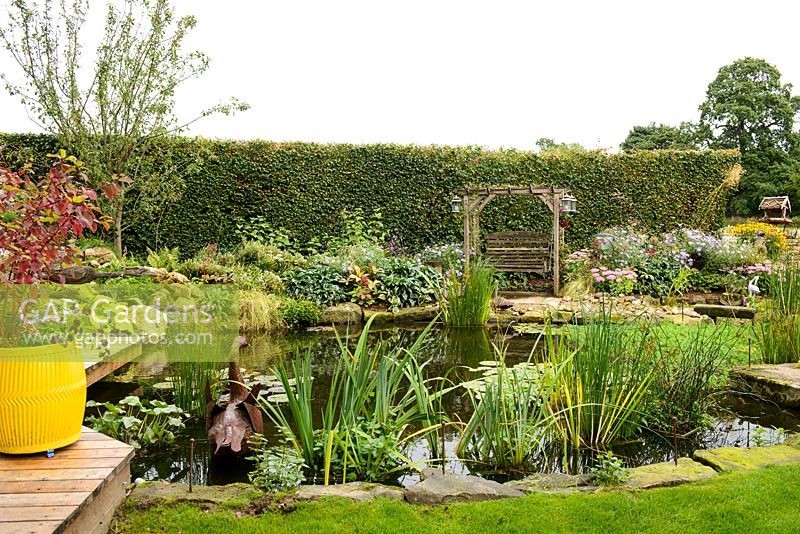 Informal pond with decking and stone edging, arbour seating and mixed planting