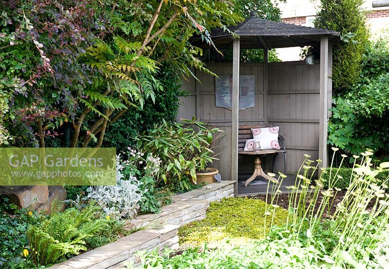 Simple wooden shelter with seating surrounded by mixed foliage planting