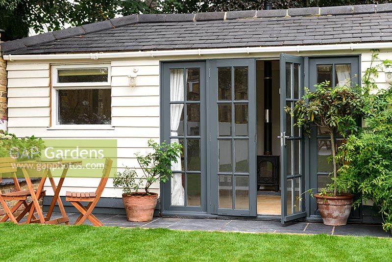 Summer house with narrow patio in front, grey painted doors and view to woodburner inside