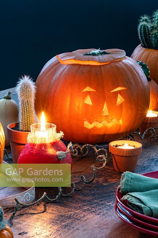 Autumnal Halloween table display with carved pumpkin, squashes, potted cacti and candles