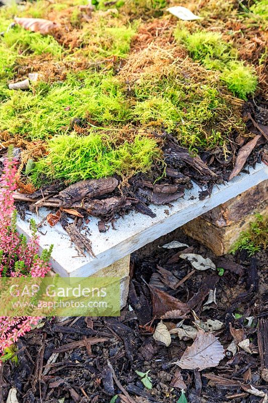 Finished hedgehog house made simply with bricks and a paving slab - camouflaged with wood chippings and moss. 