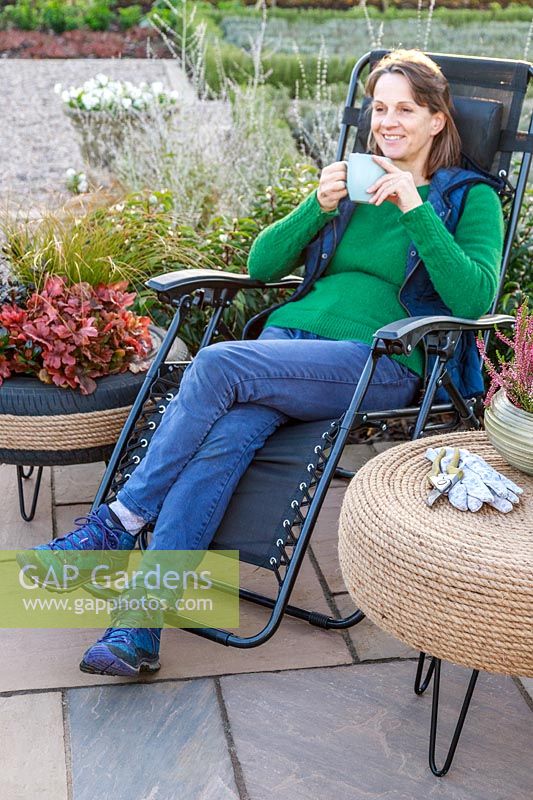 Woman sitting on reclining garden chair next to outdoor table covered with rope