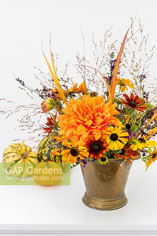 Autumnal arrangement including Rudbeckia, Helenium, Dahlia, Salvia and ornamental grasses in brass vase.