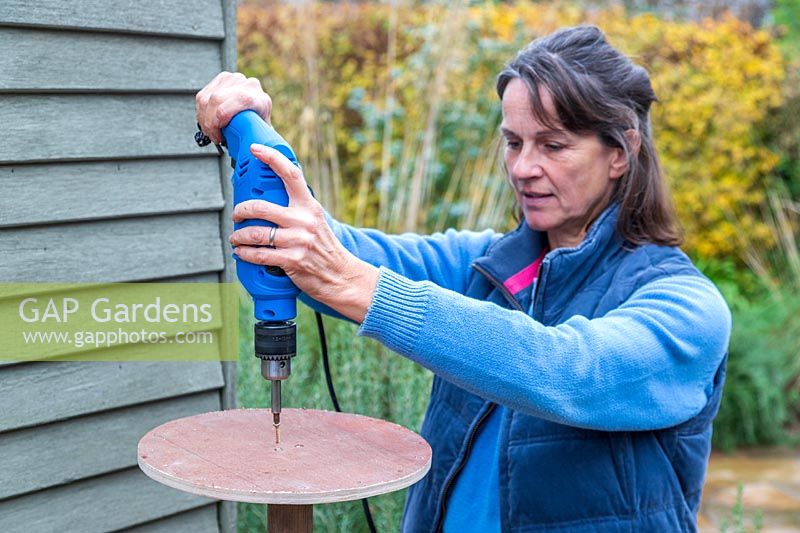 Woman using electic screwdriver to fix wooden disk to post. 