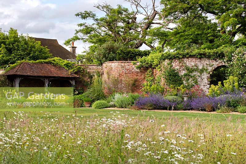 View across the wild flower meadow and main lawn towards the house and tiled pavillion by the serpentine wall. 