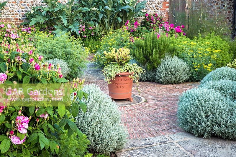 Formal herb garden in walled garden with circular paving feature and container