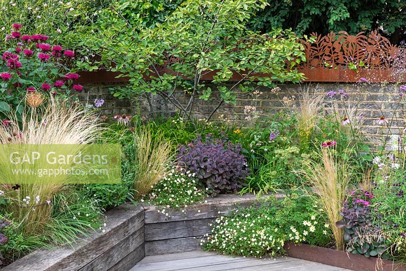Raised, wooden beds planted with ornamental grasses, Erigeron and small Amelanchier, backed by brick wall topped by corton steel panels.