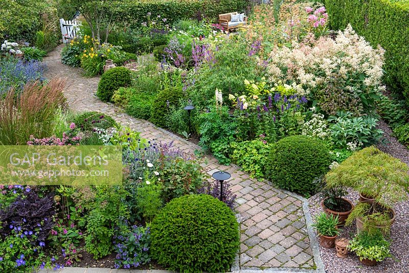 A bird's eye view of a contemporary garden design, a diagonal brick path separates a gravel garden from beds of perennials and grasses, interspersed with Taxus - Yew - ball topiary 