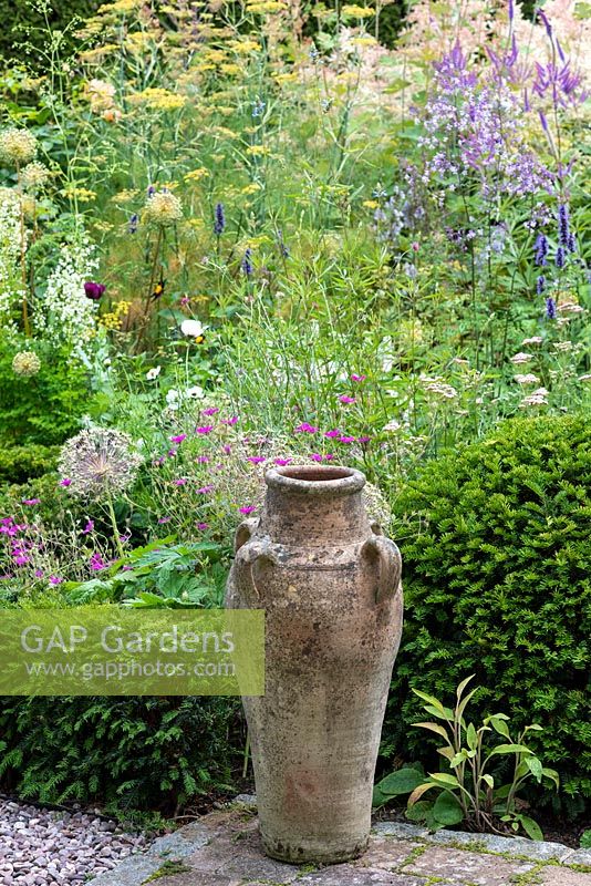 An empty urn beside a Taxus - Yew - dome, against a backdrop of hardy Geranium, Achillea, Fennel and Thalictrum 