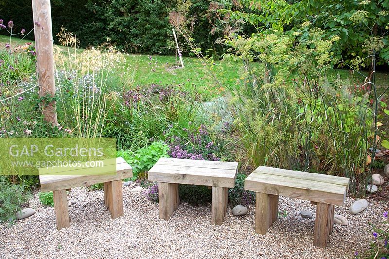 Rustic wooden seats alongside oregano, grasses and fennel  - Sedlescombe Primary School, Sussex, UK. 