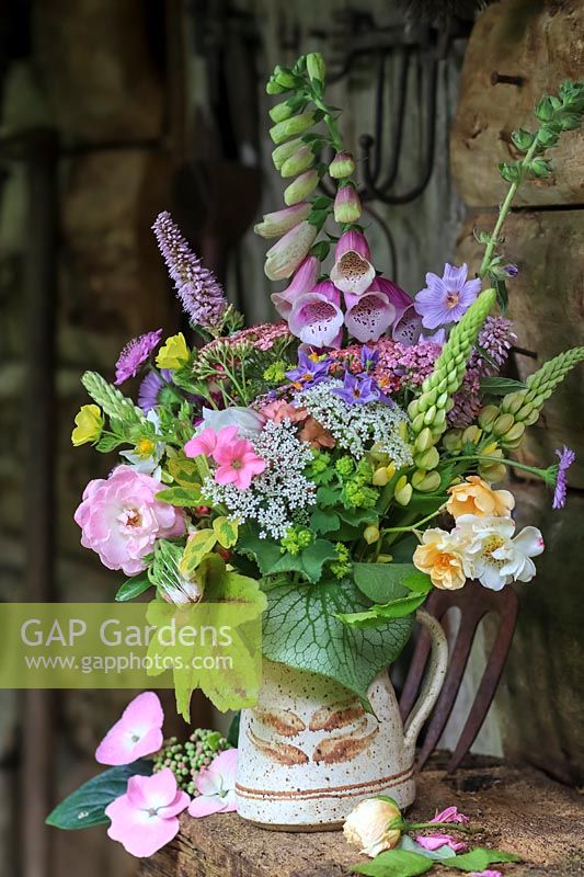 Mixed cut flowers in a jug, plants: Digitalis - Foxglove, Heucherella, Geranium, Rosa - Rose, Brunnera, Rosa 'Goldfinch' and Cow Parsley