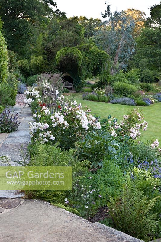 View of the garden at Mill House with, at the front, the long border with Rosa 'Felicia' and supports built using willow wands pollarded with the garden and in the distance, a large bed planted with Nepeta 'Six Hills Giant', Miscanthus x giganteus and Sanguisorba tenuifolia 'Purpurea'