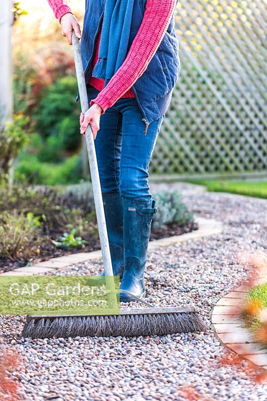 Woman using a wdie brush to level a gravel path
