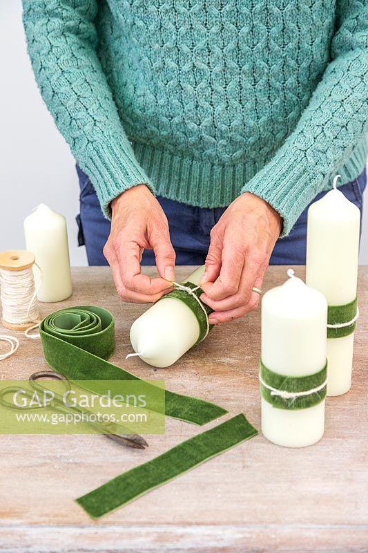 Woman adding a decorative velvet green ribbon and cream string to the pillar candle