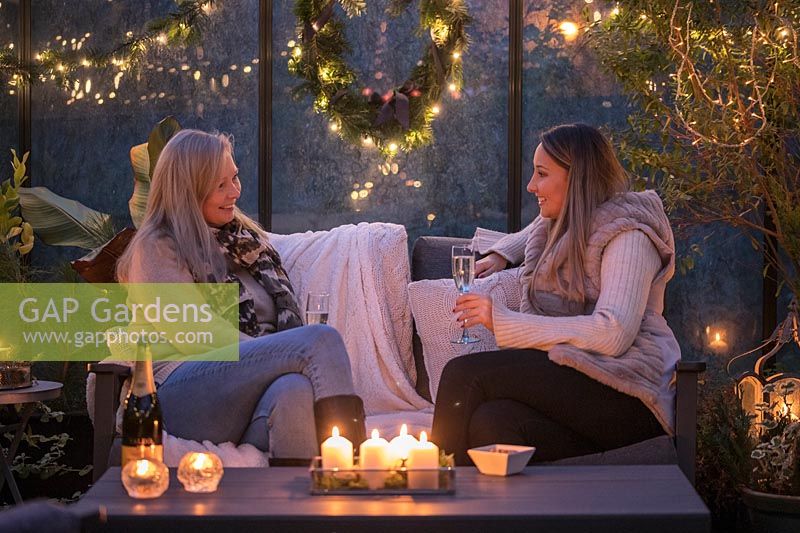 People sat in lounge furniture inside greenhouse decorated for Christmas with fairylights and candles