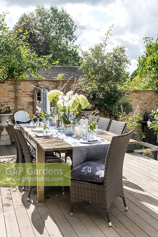Dining table dressed for alfresco dining, on wooden deck in courtyard