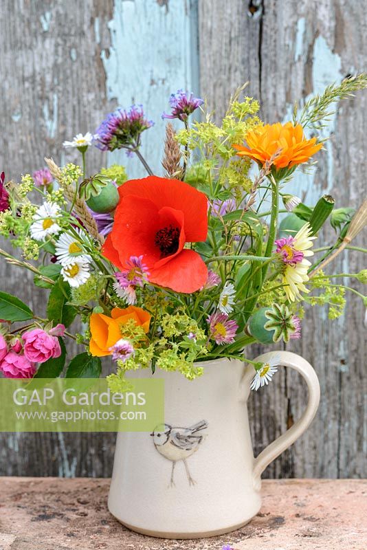 Little jug with flowers in July with Papaver rhoeas - Red poppy, Verbena bonariensis, Papaver Poppy seed heads, Calendula officinalis 'Indian Prince', Rosa roses, Alchemilla mollis, 'Erigeron karvinskianus', Annual grasses, Eschscholzia californica. Hogben pottery