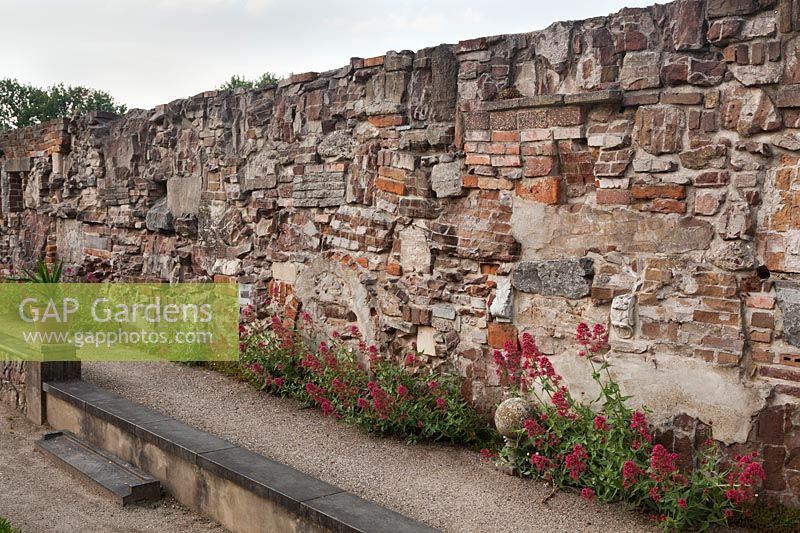 Garden wall built from various different recycled bricks and architectural stone ornaments with Centranthus ruber - Red valerian, Holland