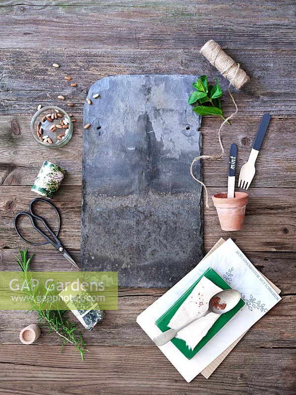 Still life with slate, scissors, seeds, paper pot maker, vintage terracotta pot and string on rustic wooden backdrop