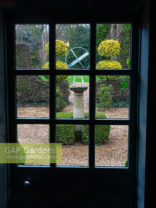 Armillary sun dial with clipped Buxus - Box - hedging and topiary, view through glass door