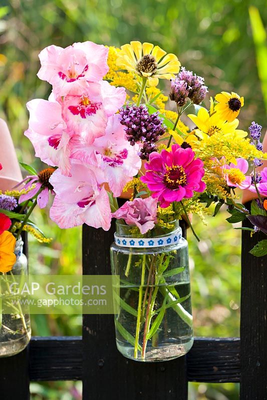 Summer flowers in a glass jar hanging on a wooden fence - Zinnia, Coneflowers, Verbena, Solidago, Gladioli.