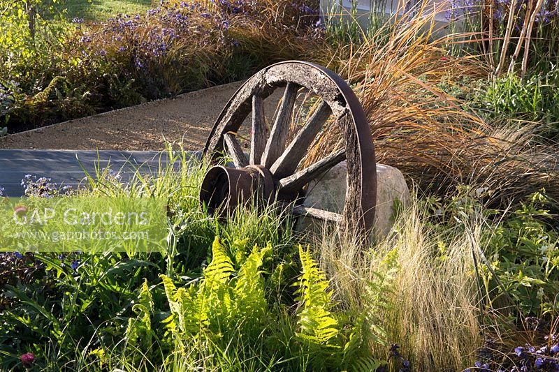 An old cart wheel in a bed with Polystichum polyblepharum, Stipa tenuissima and Polemonium 'Heaven Scent', Carex testacea and Cirsium rivulare 'Atropurpureum'. The Low Line Garden 