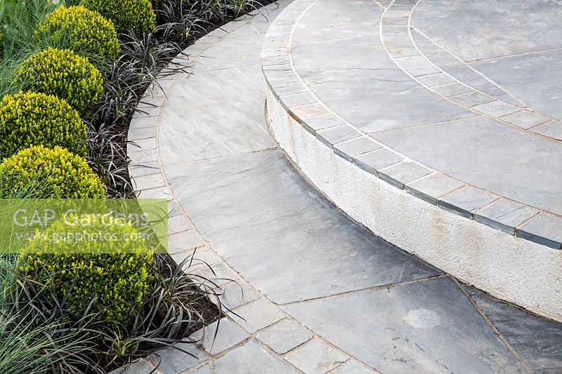 Circular paving and grey stone steps, with line of clipped Buxus sempervirens topiary balls and ornamental grasses. Hidden Gems of Worcestershire garden, RHS Malvern Spring Festival, 2016. Design: Nikki Hollier