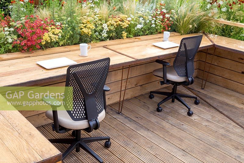 Working from home - Outdoor office work stations with wooden desks, laptop computers and office chairs by mixed planting. Prospect and Refuge garden, RHS Tatton Park Flower Show, 2017. Designer: Anca Panait 