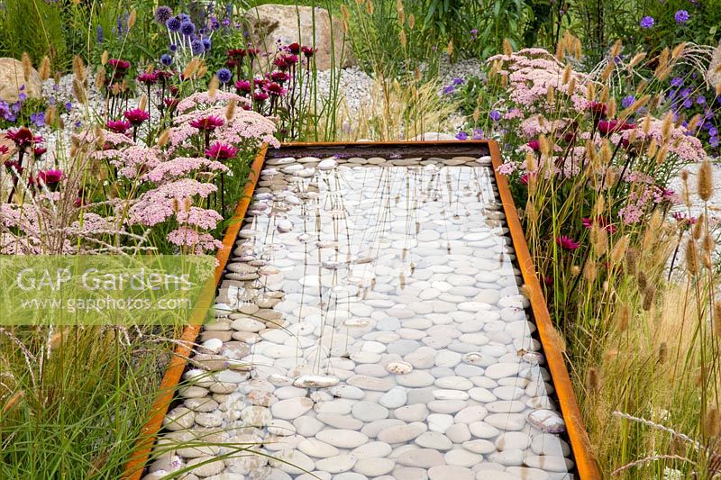Corten steel water trough water feature filled with white pebbles. Business and Pleasure Garden, RHS Tatton Park Flower Show, 2017. Designer: Jake Curley