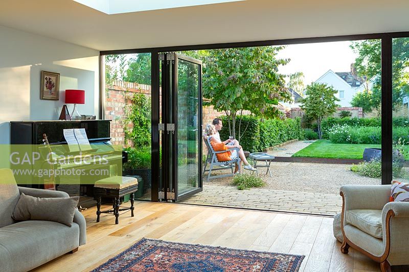 A lounge with bi-fold doors looking on to a contemporary city garden with couple relaxing on a wooden bench.