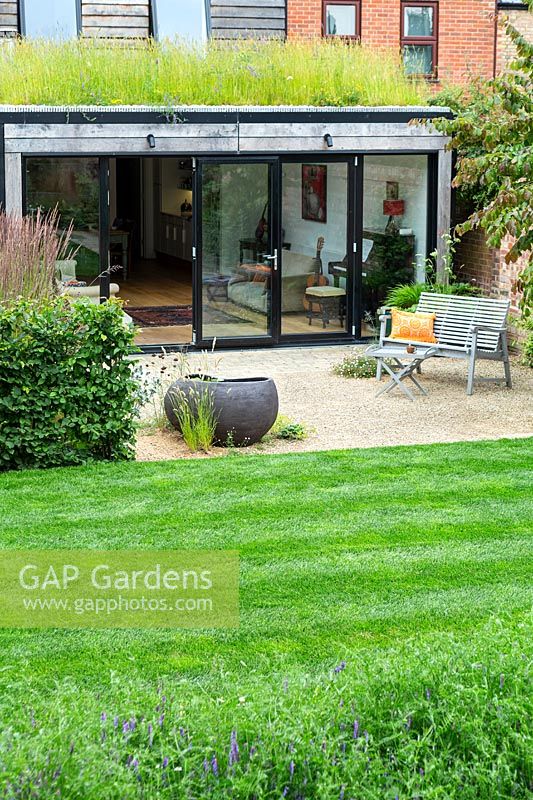 A modern house and garden with green roof, lawn, gravelled seating area and contemporary pond.