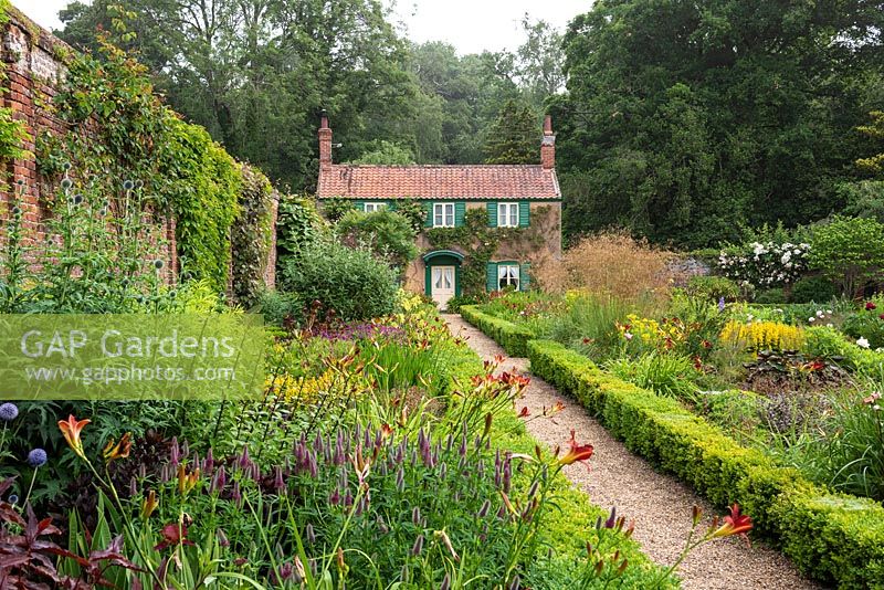 An old cottage overlooks the walled Spider Garden at Hoveton Hall. A gravel path separates herbaceous borders edged in box hedges.