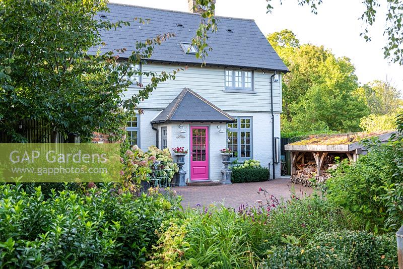 A contemporary country cottage with front garden, brick drive, wood store with green roof and mixed border planted with hydrangeas, box and perennials.